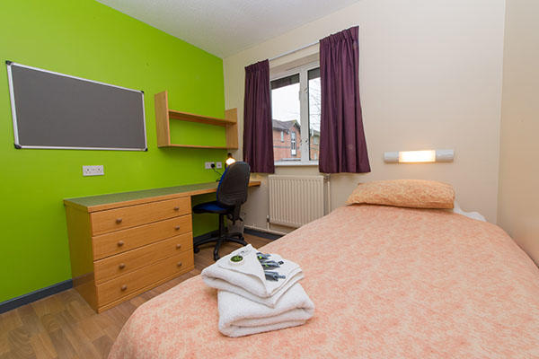 A bedroom inside Bվ accommodation. There is a single bed, a large pin board, desk, chest of drawers and a window in the room.